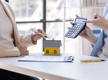 a couple of women sitting at a table with a calculator and a house